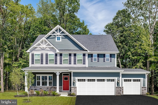 craftsman-style home featuring aphalt driveway, a shingled roof, an attached garage, a front yard, and stone siding