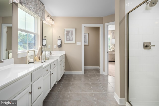 bathroom with double vanity, baseboards, tile patterned flooring, a tile shower, and a sink