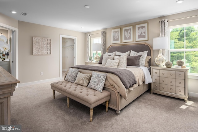 bedroom with light carpet, multiple windows, baseboards, and a walk in closet