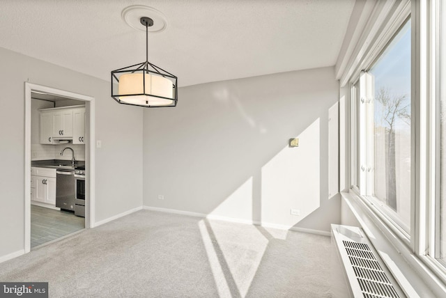 unfurnished dining area featuring light carpet, a sink, and baseboards