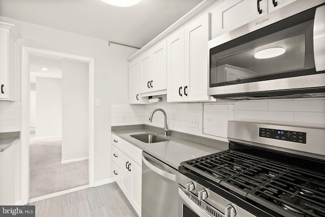 kitchen featuring light countertops, decorative backsplash, appliances with stainless steel finishes, white cabinets, and a sink