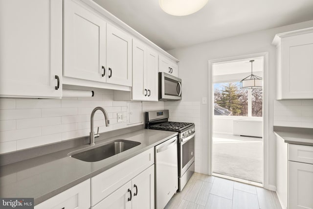 kitchen featuring stainless steel appliances, a sink, white cabinetry, tasteful backsplash, and dark countertops