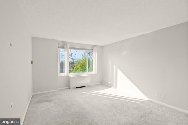 carpeted spare room with radiator, a textured ceiling, and baseboards