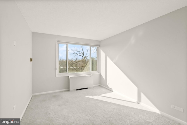 spare room featuring baseboards, carpet, and radiator