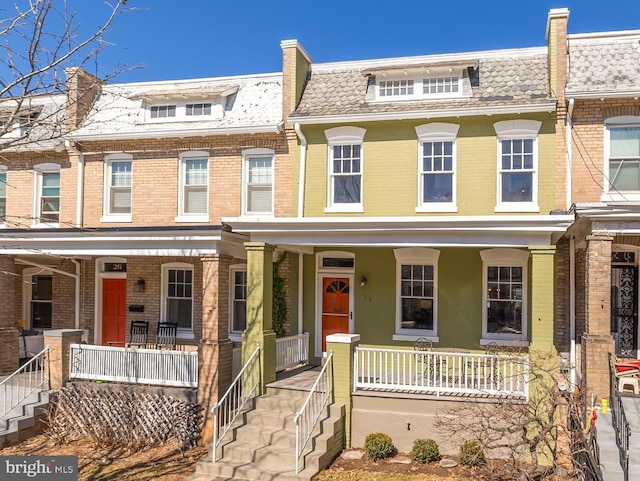 multi unit property featuring covered porch, mansard roof, and brick siding