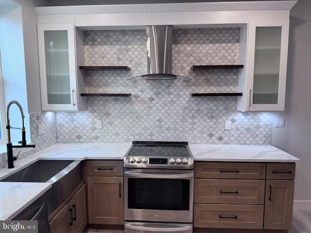 kitchen with light stone counters, a sink, wall chimney exhaust hood, stainless steel electric stove, and open shelves