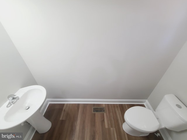 half bath featuring toilet, baseboards, visible vents, and wood finished floors