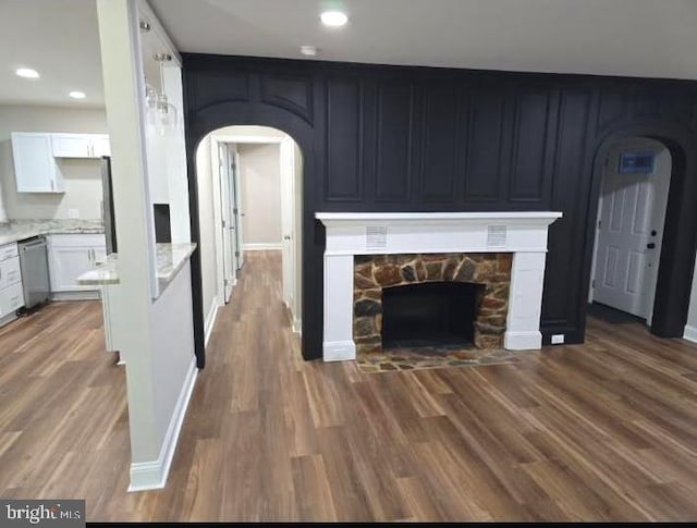 unfurnished living room featuring baseboards, arched walkways, dark wood-style flooring, a fireplace, and recessed lighting