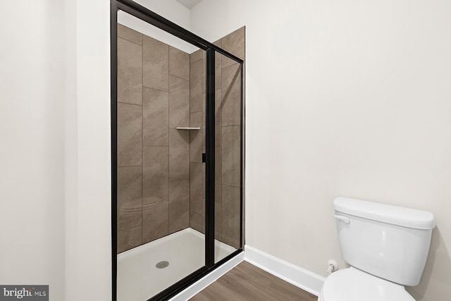 bathroom with a stall shower, toilet, baseboards, and wood finished floors