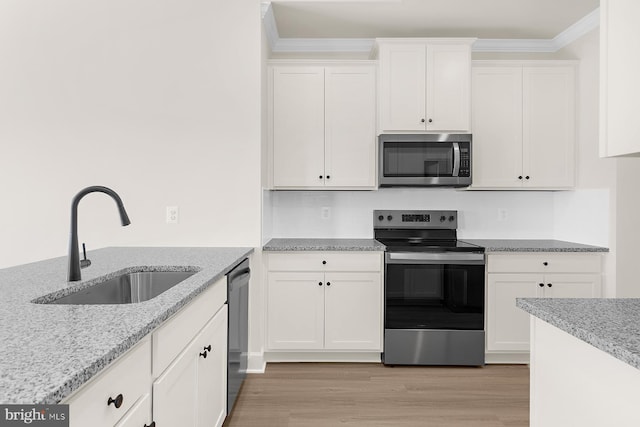 kitchen with light stone counters, a sink, white cabinetry, appliances with stainless steel finishes, and light wood-type flooring