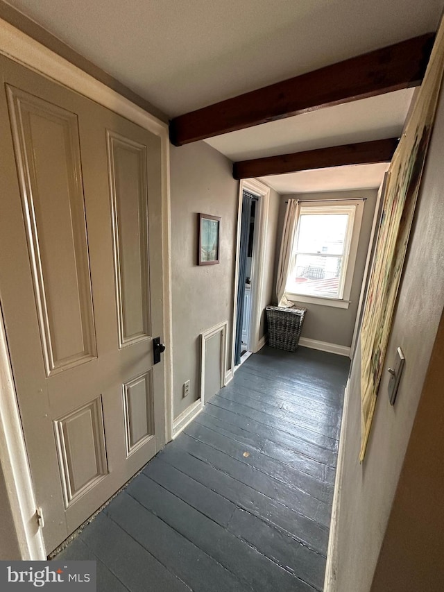 hallway featuring dark wood-style flooring, beamed ceiling, and baseboards