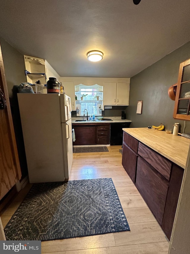 kitchen featuring light countertops, light wood-style flooring, freestanding refrigerator, a sink, and dark brown cabinetry