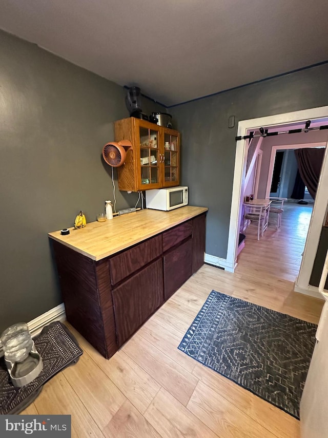 bar with white microwave, light wood-style flooring, and baseboards