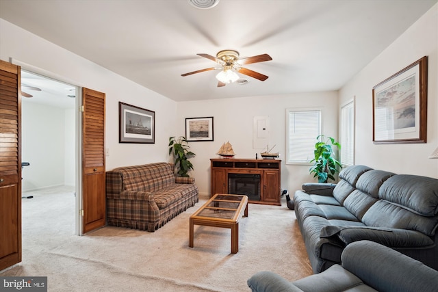 living room with a glass covered fireplace, a ceiling fan, and light colored carpet