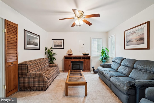 living room featuring a ceiling fan, a glass covered fireplace, and light colored carpet