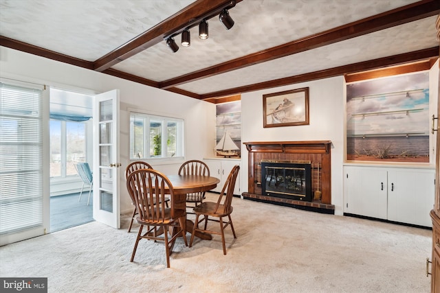 carpeted dining area with beamed ceiling, a fireplace, and rail lighting