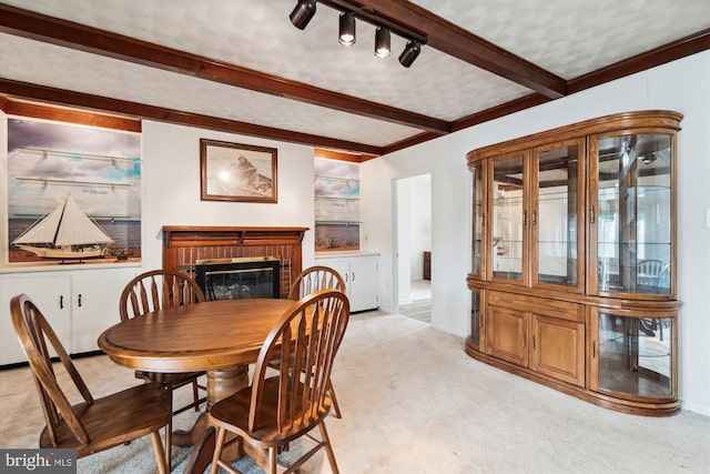 dining space with light carpet, a fireplace, track lighting, and beam ceiling