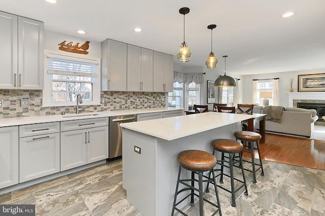 kitchen with gray cabinetry, a breakfast bar, a sink, stainless steel dishwasher, and a center island