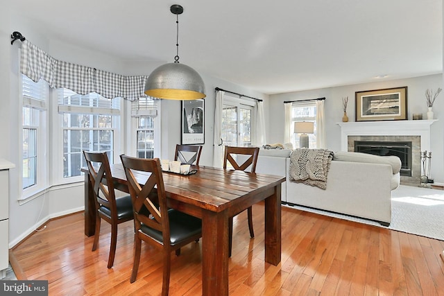 dining area with light wood-type flooring, a tiled fireplace, and baseboards