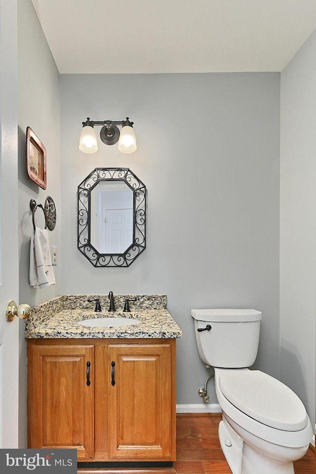 half bath featuring baseboards, vanity, toilet, and wood finished floors