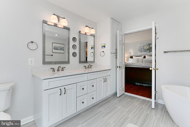 ensuite bathroom with double vanity, toilet, ensuite bathroom, a freestanding bath, and a sink