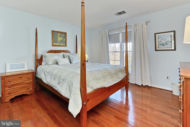 bedroom with baseboards, visible vents, and wood finished floors