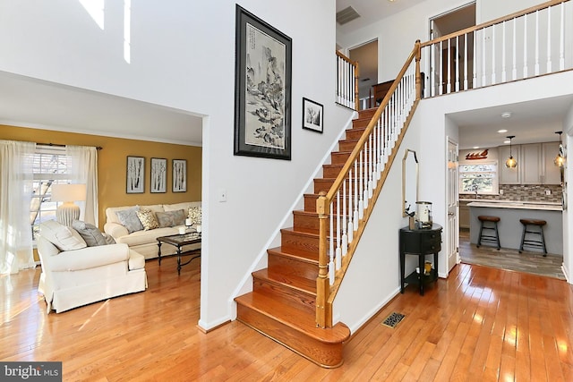 stairs with baseboards, visible vents, a towering ceiling, and hardwood / wood-style floors