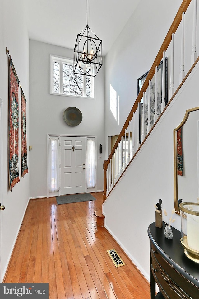 entryway featuring visible vents, light wood-style flooring, a high ceiling, and stairs