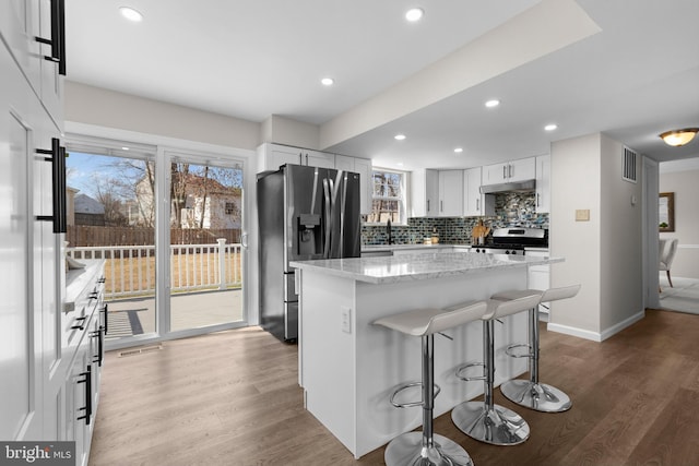 kitchen featuring under cabinet range hood, visible vents, appliances with stainless steel finishes, backsplash, and plenty of natural light