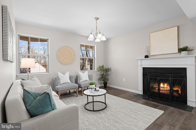 living area featuring a warm lit fireplace, a notable chandelier, baseboards, and wood finished floors