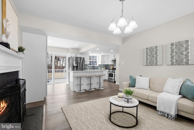 living room featuring a warm lit fireplace, recessed lighting, wood finished floors, and a chandelier