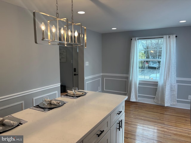 interior space with a chandelier, a decorative wall, a wainscoted wall, wood finished floors, and white cabinets