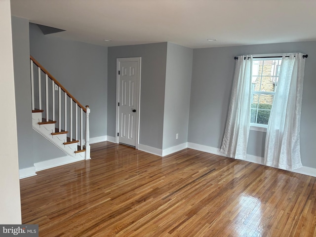 spare room featuring baseboards, stairway, and wood finished floors