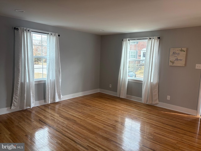 empty room featuring a wealth of natural light, baseboards, and wood finished floors