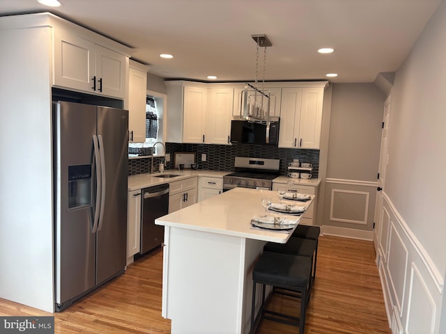 kitchen with light wood finished floors, a sink, stainless steel appliances, light countertops, and backsplash