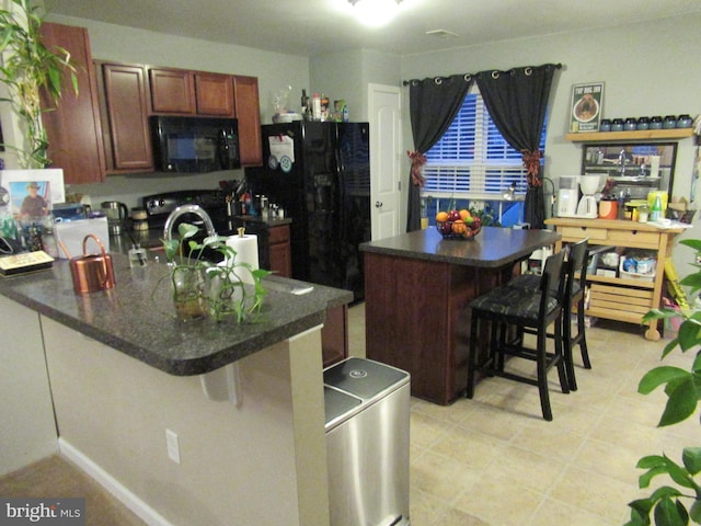 kitchen with washer and clothes dryer, a breakfast bar area, dark countertops, a peninsula, and black appliances