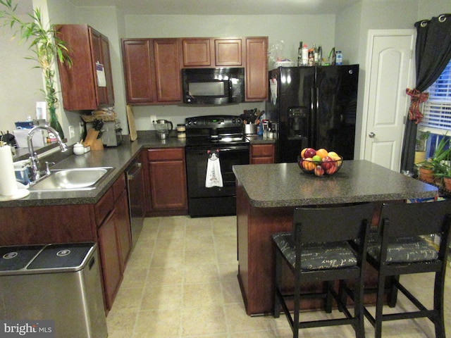 kitchen featuring dark countertops, a kitchen island, a breakfast bar area, black appliances, and a sink