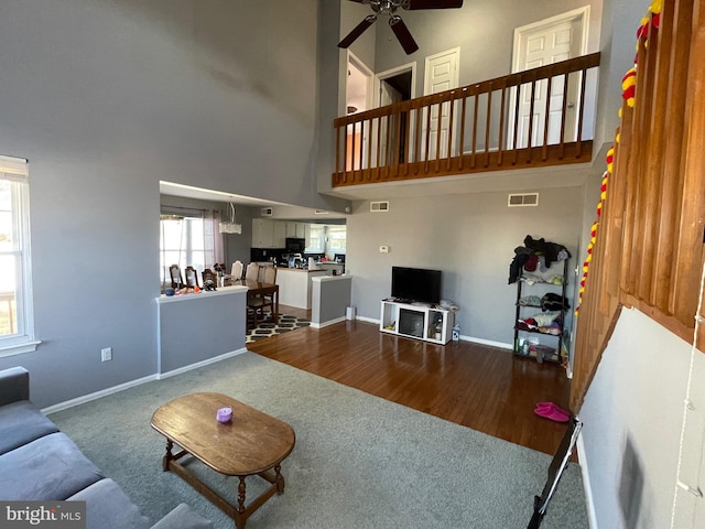 living area featuring ceiling fan, a high ceiling, visible vents, and baseboards