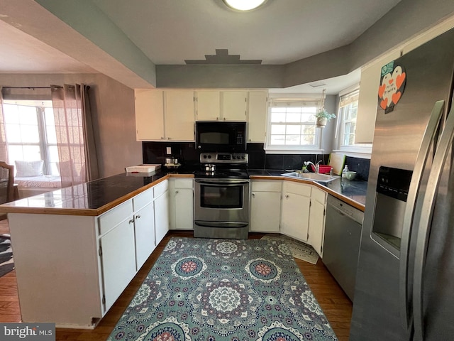 kitchen featuring dark wood finished floors, appliances with stainless steel finishes, a peninsula, white cabinetry, and a sink