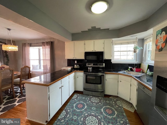 kitchen with pendant lighting, an inviting chandelier, appliances with stainless steel finishes, a sink, and a peninsula