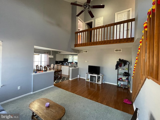 living area with visible vents, baseboards, a towering ceiling, dark wood-style floors, and ceiling fan