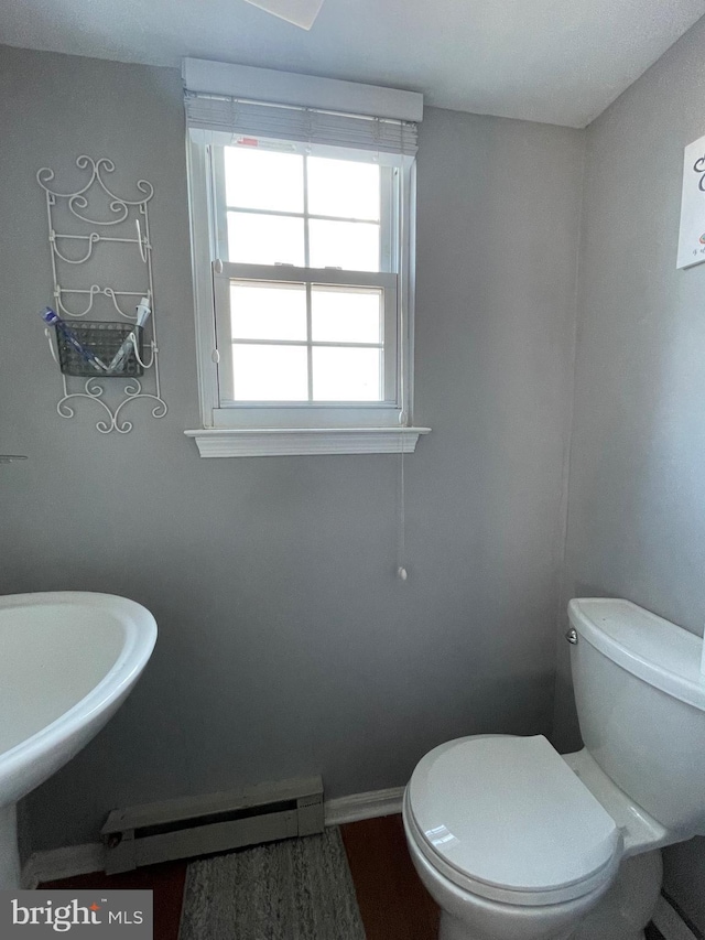 half bath with a baseboard heating unit, baseboards, and toilet