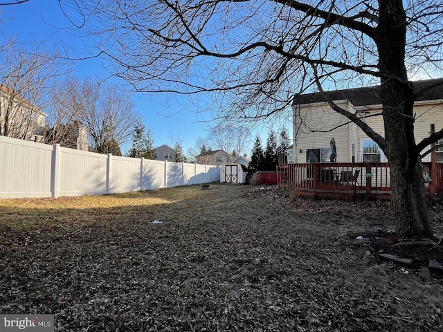 view of yard with an outbuilding, a storage unit, a fenced backyard, and a deck