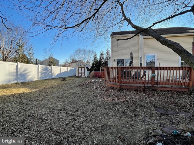 view of yard featuring an outbuilding, a fenced backyard, a deck, and a storage shed