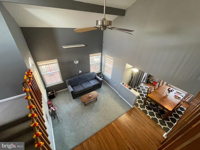 living area with baseboards, a towering ceiling, ceiling fan, wood finished floors, and beamed ceiling