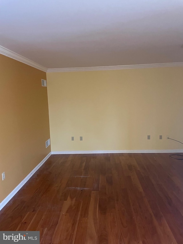 empty room with visible vents, baseboards, wood finished floors, and crown molding