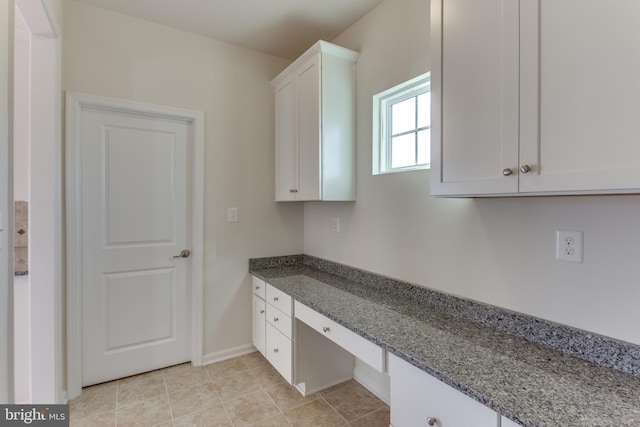 kitchen with light tile patterned floors, white cabinets, dark stone countertops, and built in study area