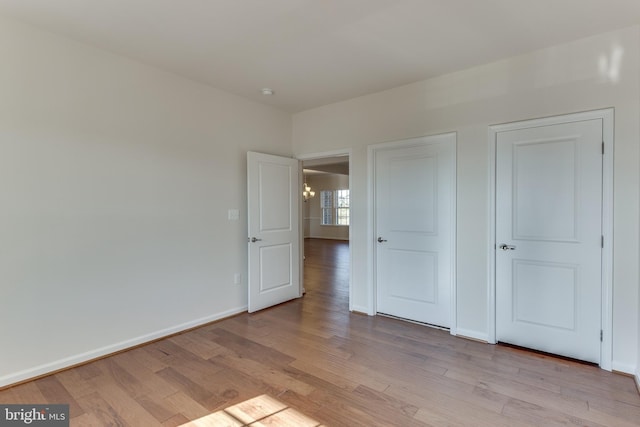 unfurnished bedroom with light wood-style floors, a notable chandelier, and baseboards