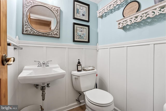 bathroom featuring a wainscoted wall, toilet, a decorative wall, and a sink