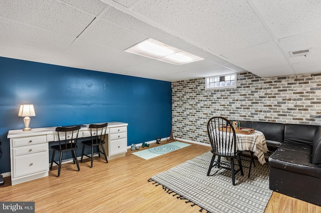 home office with visible vents, brick wall, baseboards, wood finished floors, and a paneled ceiling